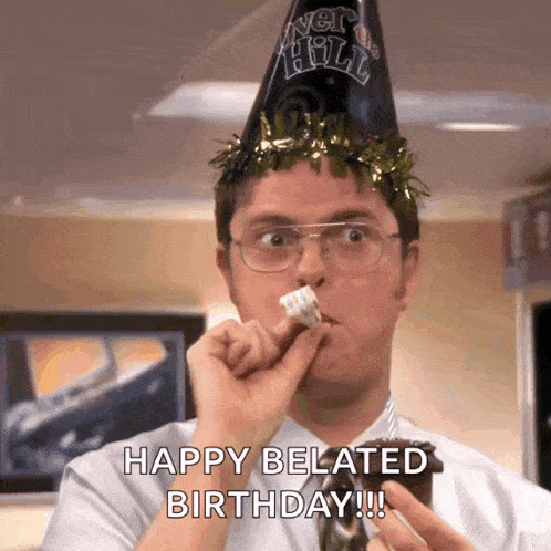 a man wearing a party hat is eating a cake and saying happy belated birthday !!!