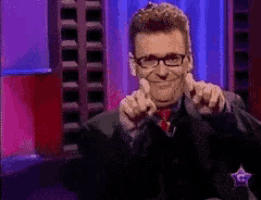 a man wearing glasses and a black suit is pointing at the camera