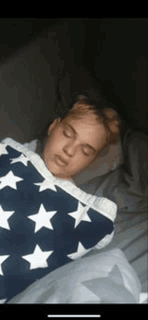 a young boy is sleeping on a bed with a blue and white american flag blanket .