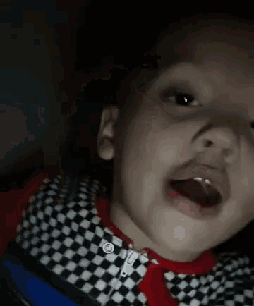 a close up of a child 's face with his mouth open and a checkered shirt on .
