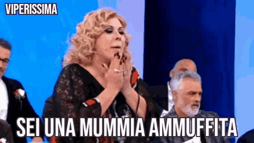 a woman is sitting in front of a group of men and says sei una mummia ammuffita