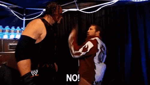 two wrestlers are pointing at each other and one of them is saying no .