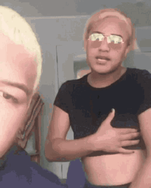 two men are standing next to each other and one of them is wearing sunglasses and a crop top .