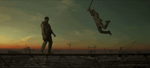 a man is standing on a bridge while another man is flying in the air