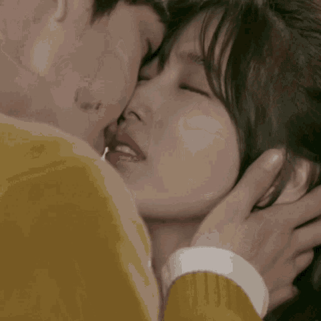 a man in a yellow shirt kisses a woman with a tattoo on his face
