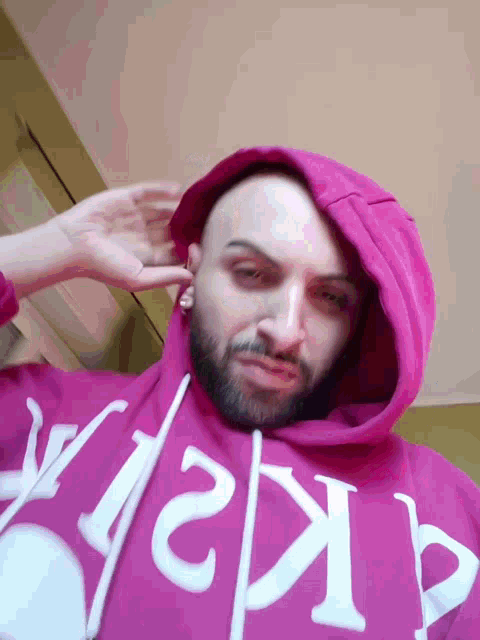 a man with a beard wears a pink hoodie with the letters a and k on it