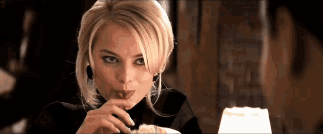 a woman with blonde hair is sitting at a table with a lamp in the background