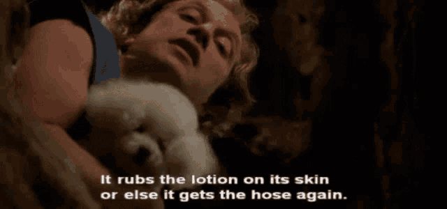 a man is holding a small white dog and says it rubs the lotion on its skin or else it gets the hose again .