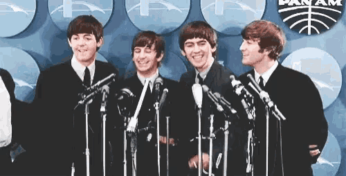 the beatles are standing in front of microphones and smiling at the camera .
