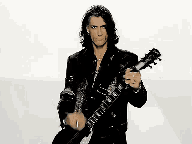 a man in a black jacket is holding a gibson electric guitar
