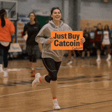 a woman is running on a basketball court holding an orange sign that says just buy catcoin