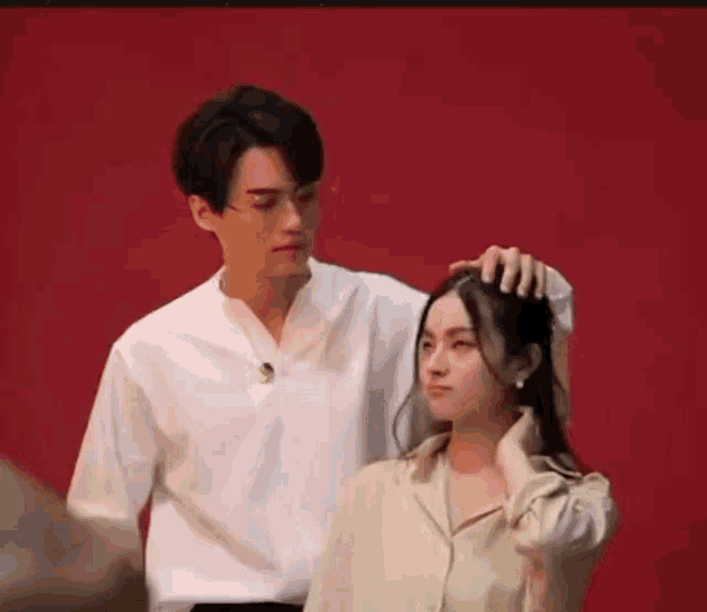 a man and a woman are standing next to each other . the man is touching the woman 's hair .