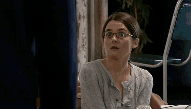 a woman wearing glasses and a grey sweater is sitting at a table