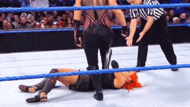 a woman laying on the ground in a wrestling ring with a referee in the background