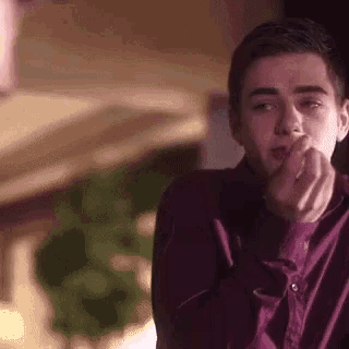 a young man in a purple shirt is eating a piece of food from his hand .