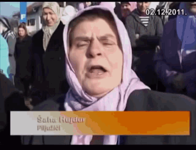 a woman wearing a head scarf stands in front of a crowd with the date 02.12.2011 on the bottom