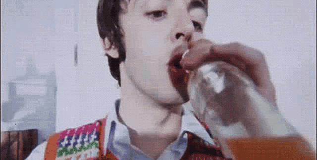 a man is drinking from a glass while wearing a sweater vest
