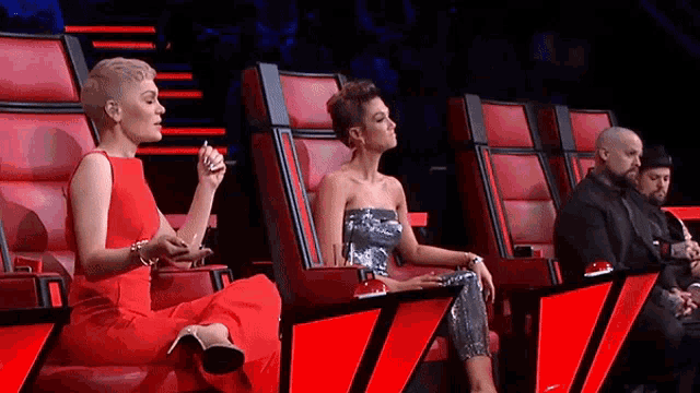 a woman in a red dress is sitting in a red chair talking to another woman .