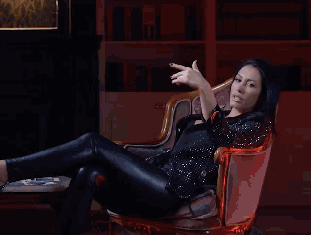 a woman in a leather jacket sits in a chair with her legs crossed