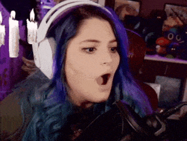 a woman with purple hair is wearing headphones and a microphone and making a surprised face .