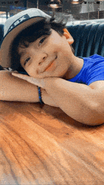 a young boy wearing a hat and a blue shirt is sitting at a table with his head resting on his hands