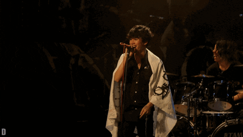 a man singing into a microphone in front of a drum set that says tama on it