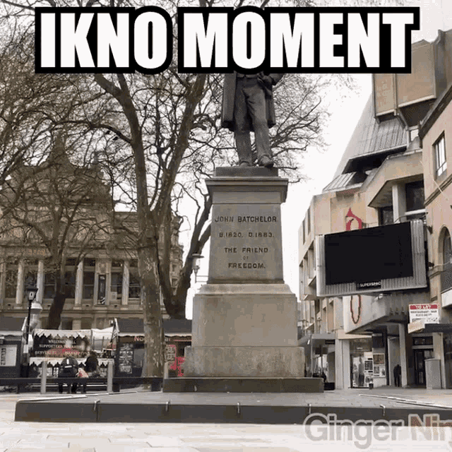 a statue of john batchelor sits in front of a sign that says " ikno moment "