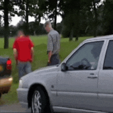 a man in a red shirt stands next to a car