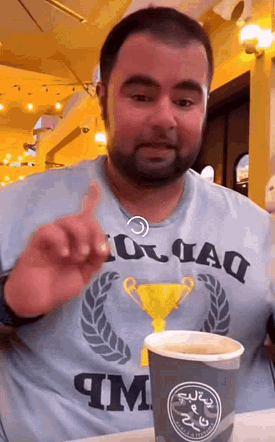 a man with a beard wearing a shirt that says squad is sitting at a table with a cup of coffee