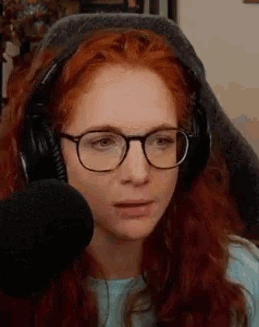 a woman with red hair and glasses is wearing headphones and looking at the camera .
