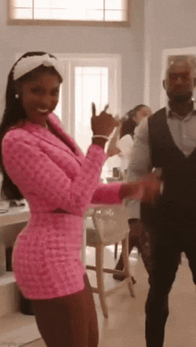 a woman in a pink dress is dancing with a man in a suit in a living room .