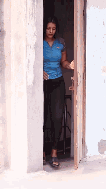 a woman in a blue shirt and black pants opens a door