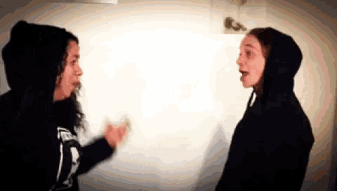 two women are standing next to each other in front of a white wall .