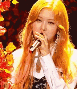 a woman with long blonde hair is singing into a microphone on stage .