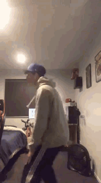a man wearing a hat and a hoodie is standing in a room .