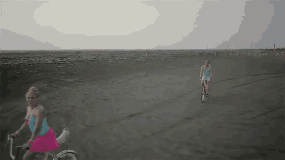 a woman in a blue tank top is riding a bike on a dirt road