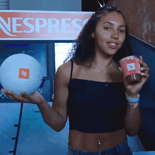 a woman holding a cup of coffee and a basketball in front of a sign that says nespress