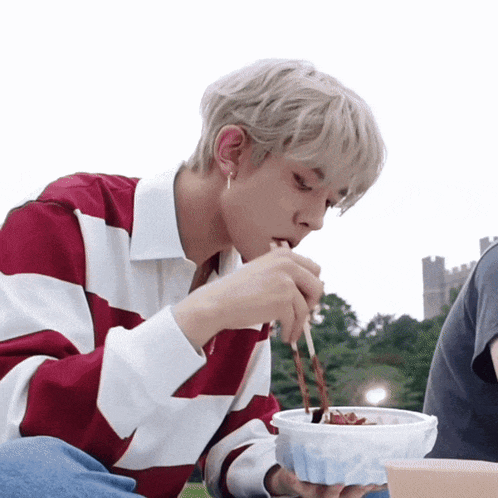 a man wearing a red and white striped shirt is eating a bowl of food with chopsticks