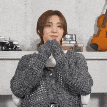 a woman wearing a grey sweater and gloves is sitting in front of a fireplace .