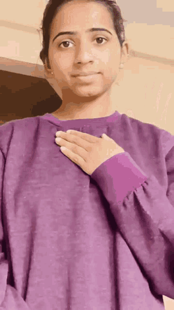 a woman in a purple sweater is holding her hand to her chest .