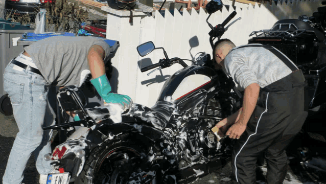 two men washing a motorcycle with a license plate that says fr