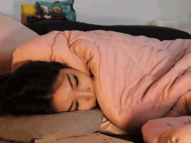 a woman wrapped in a pink blanket is sleeping on a pillow