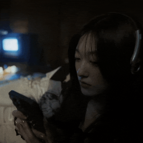 a woman wearing headphones is looking at her phone in the dark