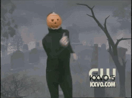 a man with a pumpkin head is dancing in front of a cemetery