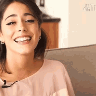 a woman is smiling while sitting on a couch with a microphone .