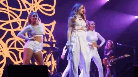 a woman in a white dress is standing on a stage with a group of dancers .