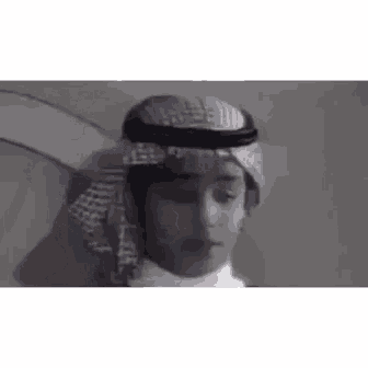 a man wearing a turban and scarf is talking in arabic .
