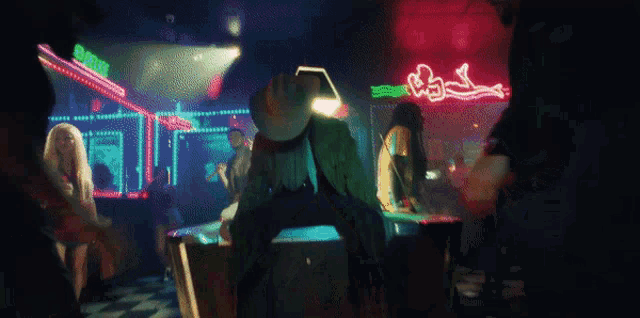 a man in a cowboy hat sits on a table in front of a neon sign that says ' show '