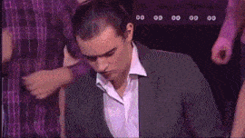 a man in a suit and white shirt is standing in front of a purple wall with numbers 00 and 00 on it