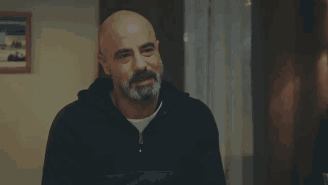 a bald man with a beard wears a black sweatshirt